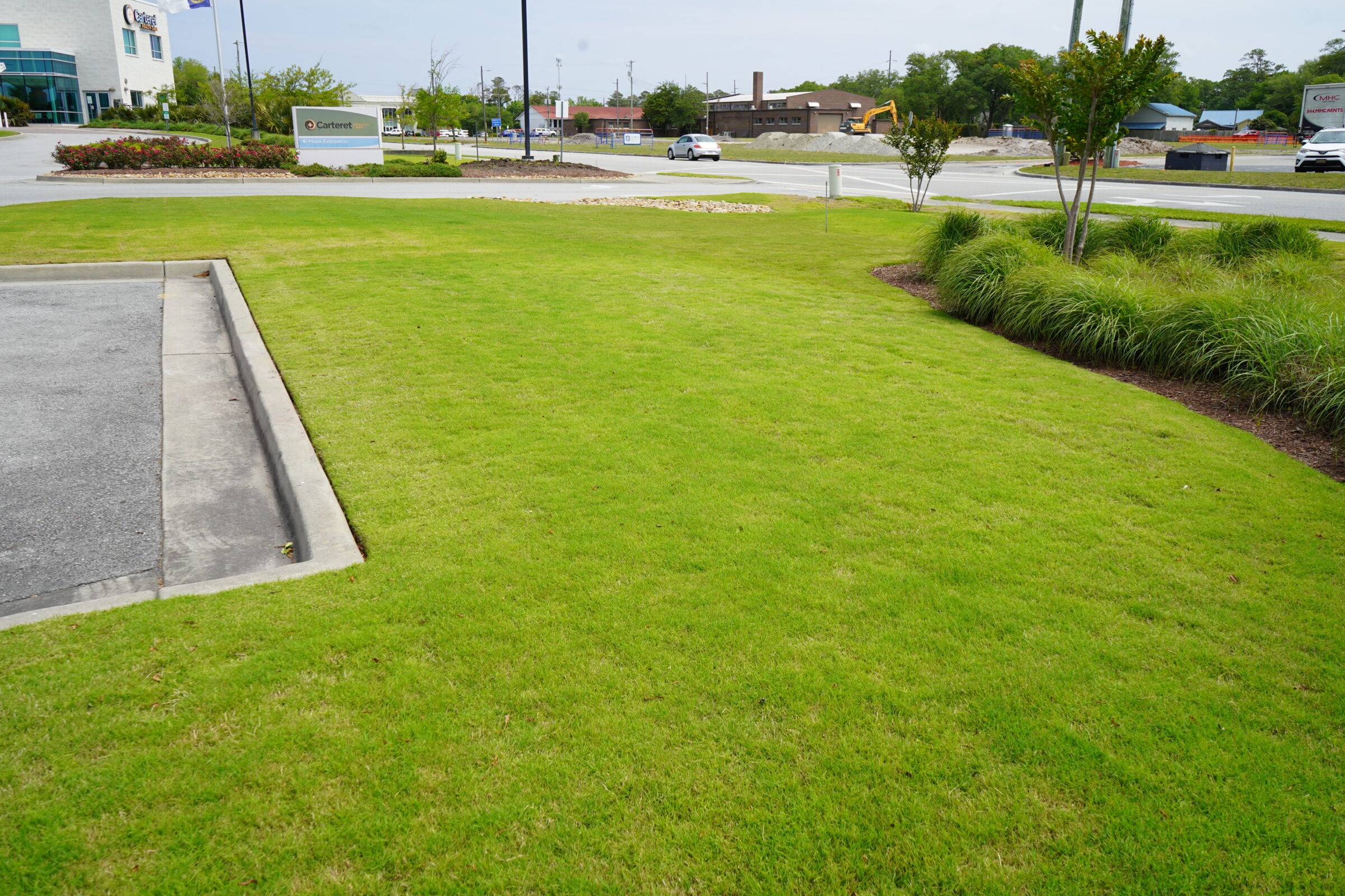 Lush green lawn with a parking lot and a building in the background; "Carteret" sign visible near the road.