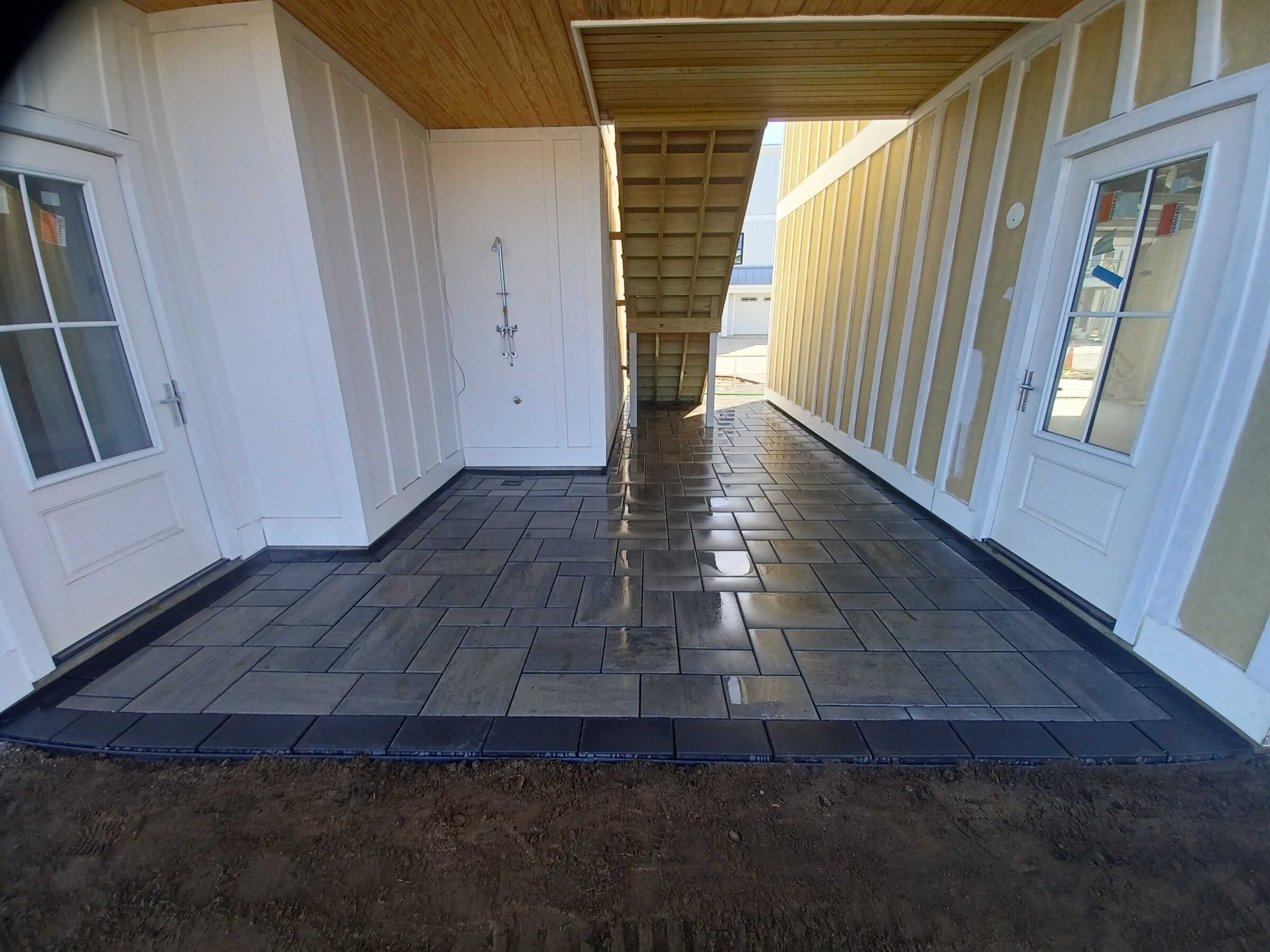 A modern passageway with tiled flooring, two white doors, a shower fixture, and wooden stairs leading to the upper level.