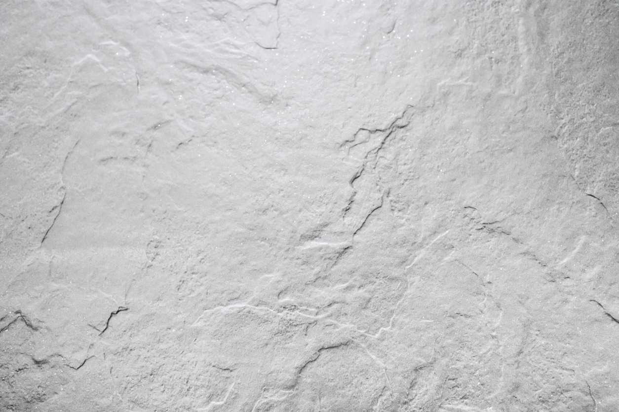 Close-up of a textured, light-colored stone surface with natural, uneven patterns and subtle, faint lines across the entire expanse.